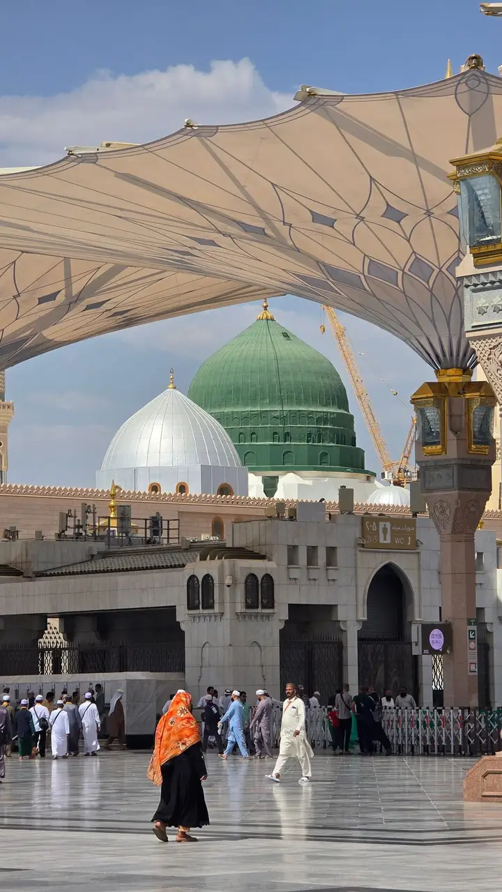 The Green Dome of Al-Masjid an-Nabawi beneath the courtyard canopies as pilgrims pass, in Madina